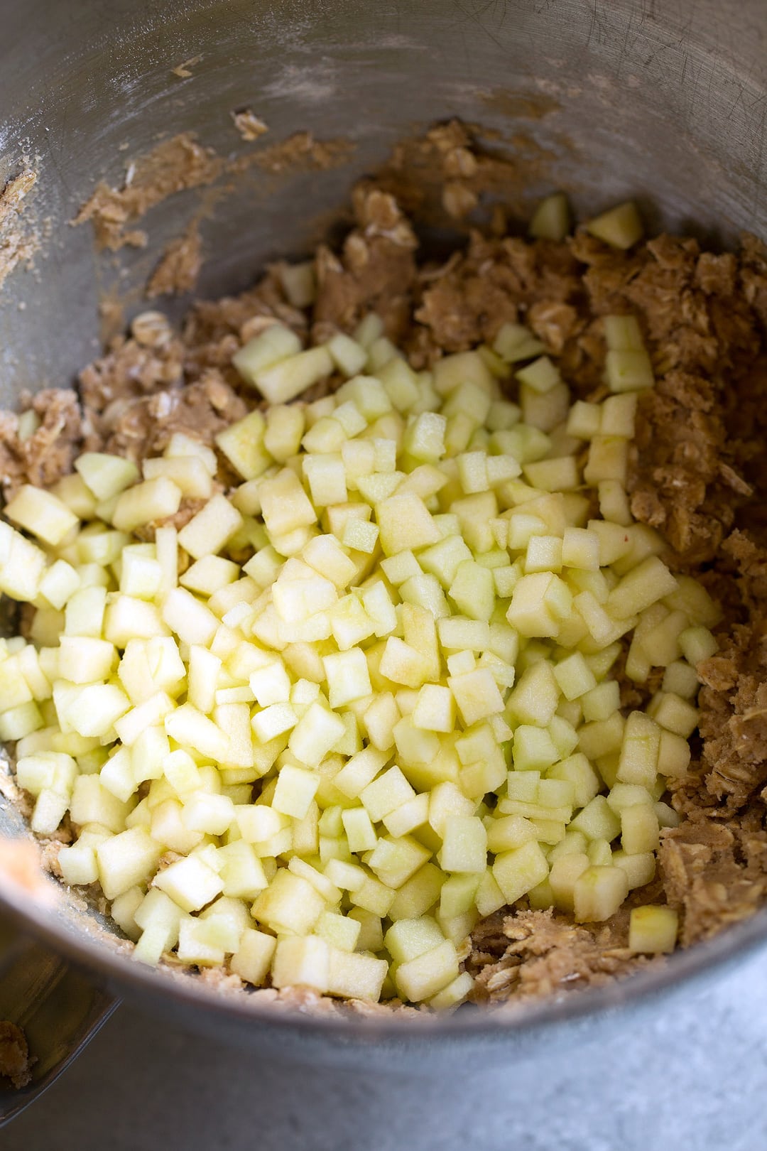 Image of diced bits of apples over cookie dough in a mixing bowl.