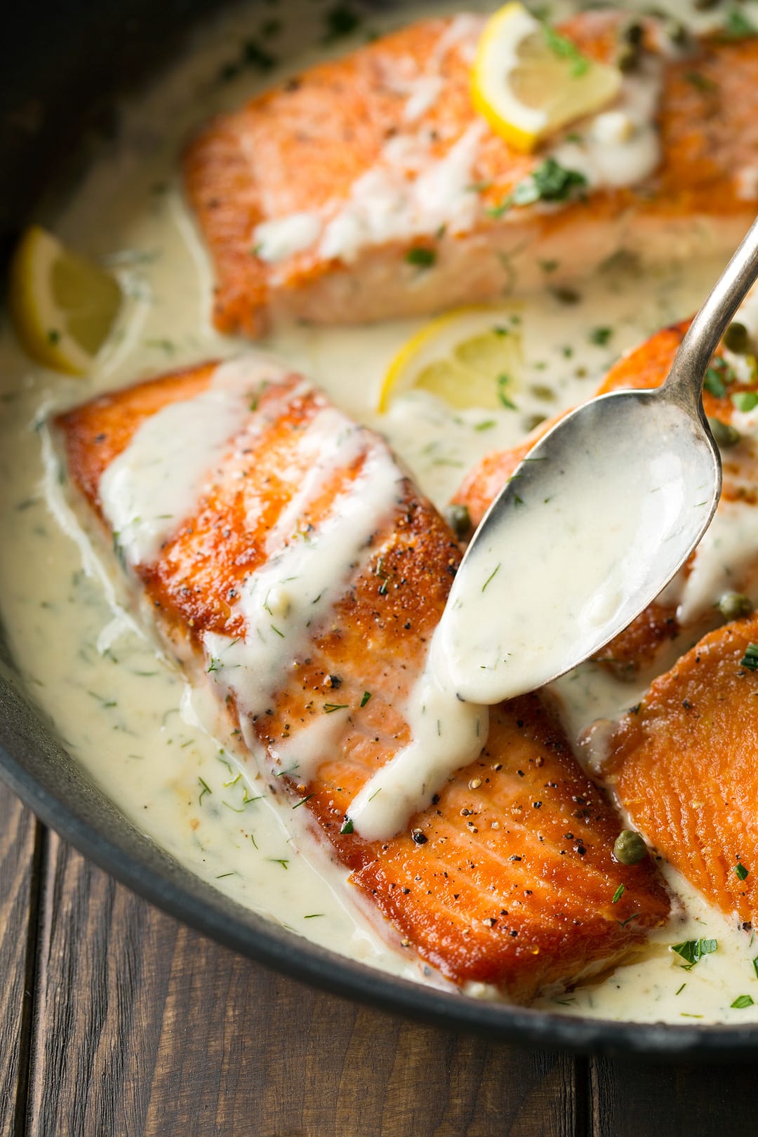 Salmon recipe cooked in a skillet with creamy lemon dill sauce over the top.