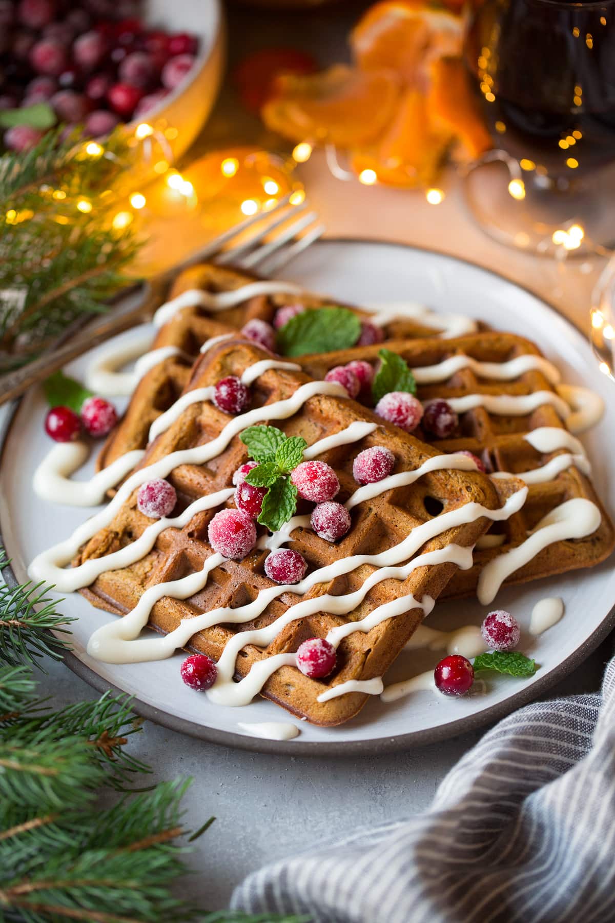 Gingerbread Waffles for Christmas breakfast. Shown here on a serving plate with pine and Christmas lights around waffles.