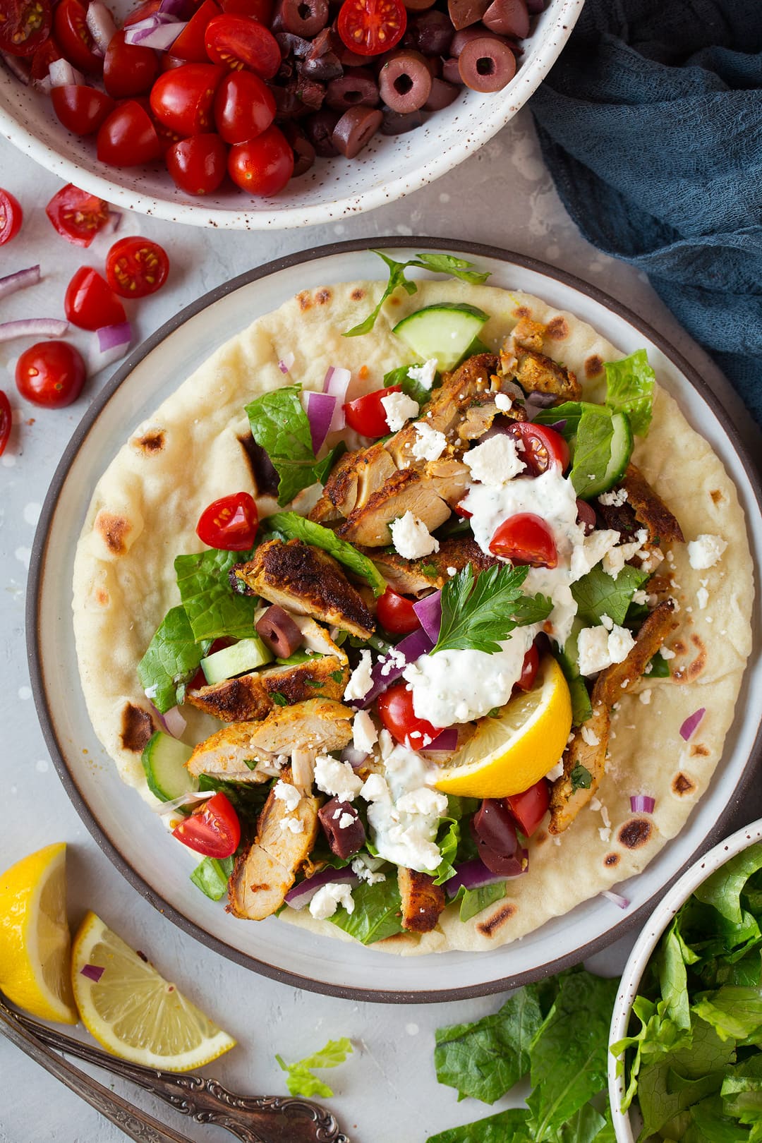 Chicken Shawarma layered over pita bread with various toppings including lettuce, tomatoes, feta, red onion, and a tahini sauce