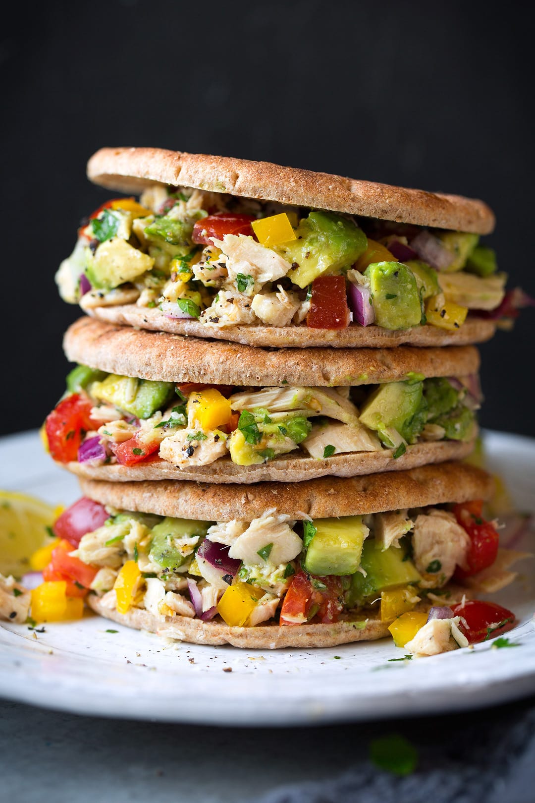 Avocado Tuna Salad shown in a stack of three, served between sandwich thin buns, on a white plate 