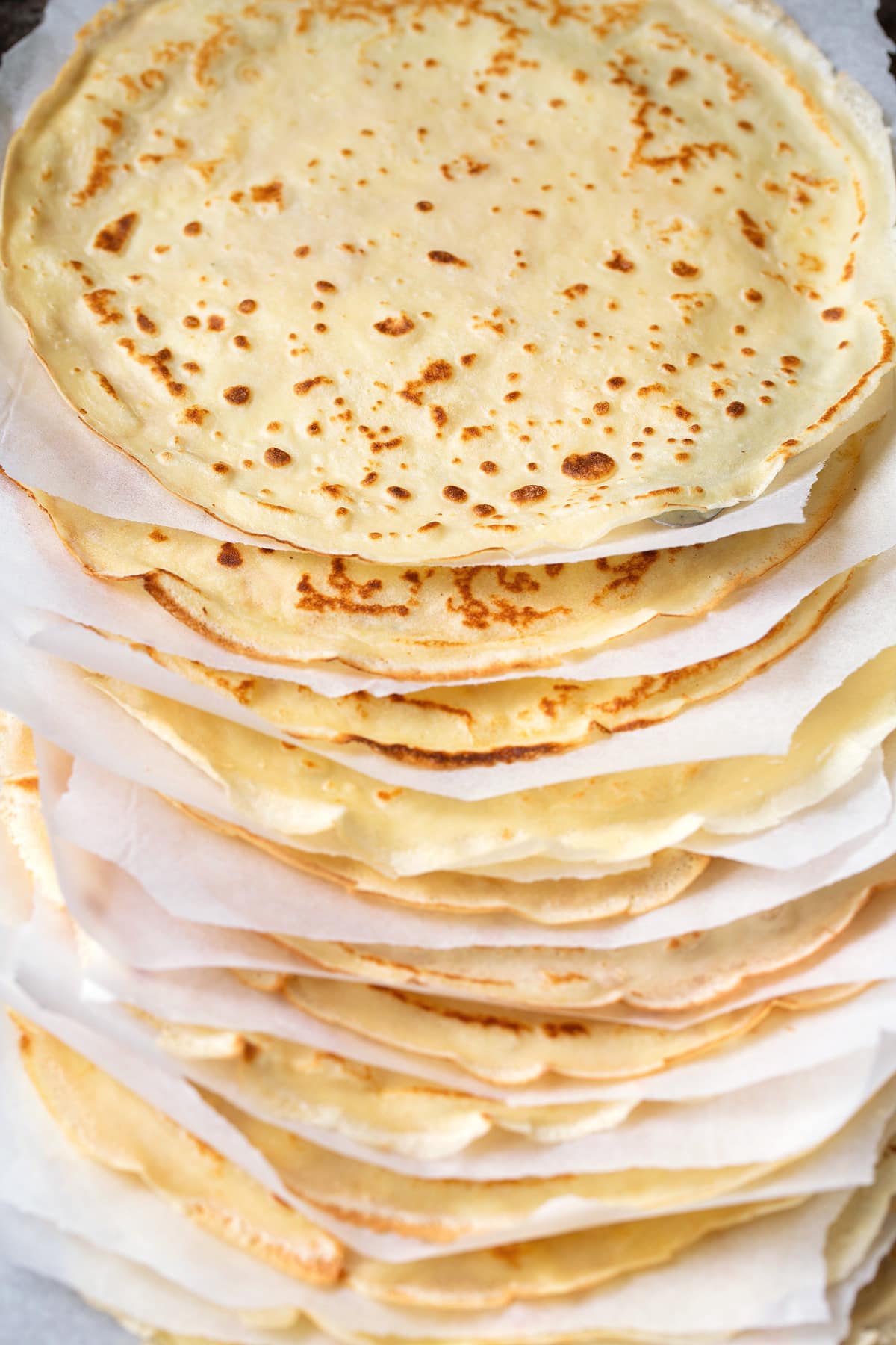 Stack of homemade crepes with parchment paper between each.