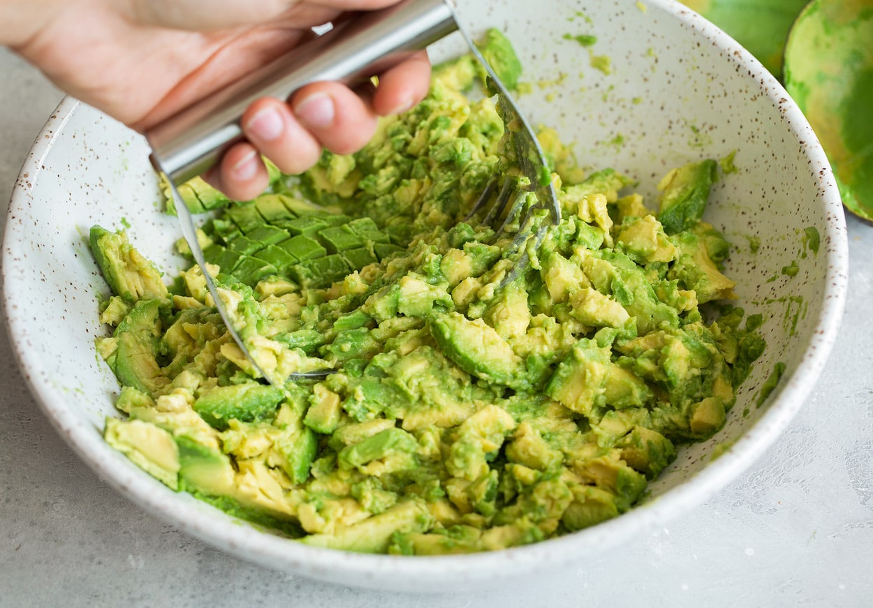 Mashing avocados in a mixing bowl using pastry cutter to make homemade guacamole.