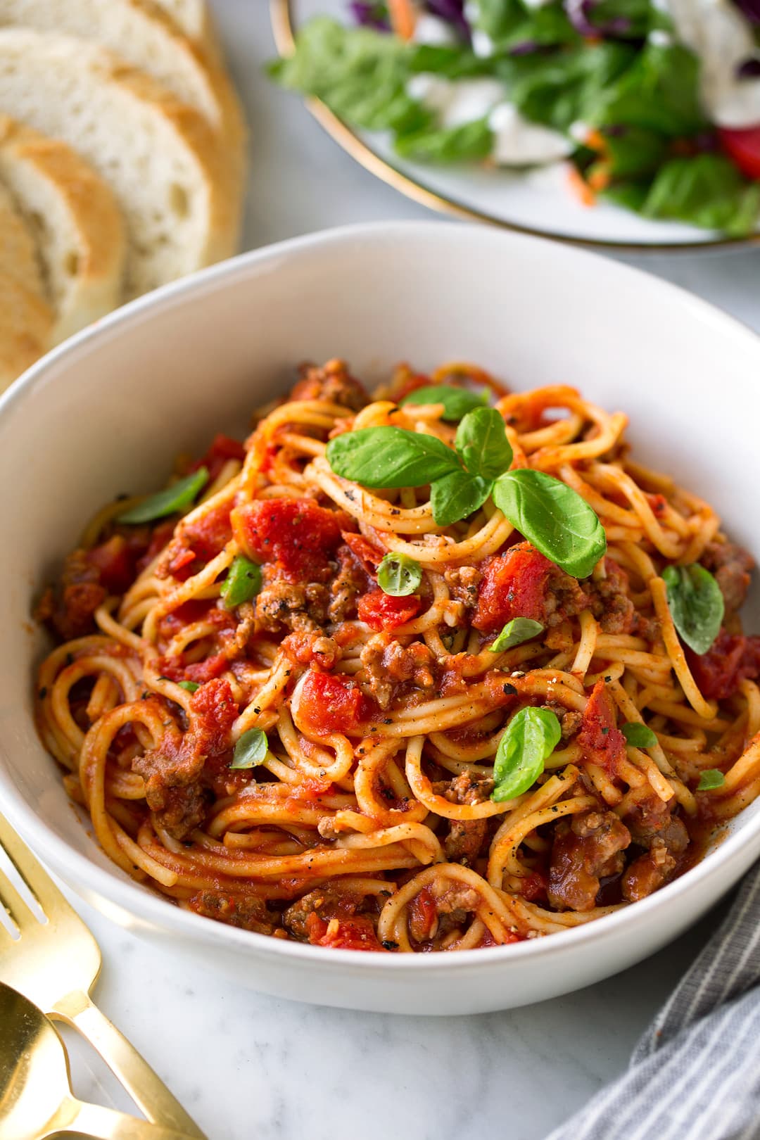 Instant Pot Spaghetti shown here in a single serving in a white pasta bowl with fresh bread and a side salad in the background.