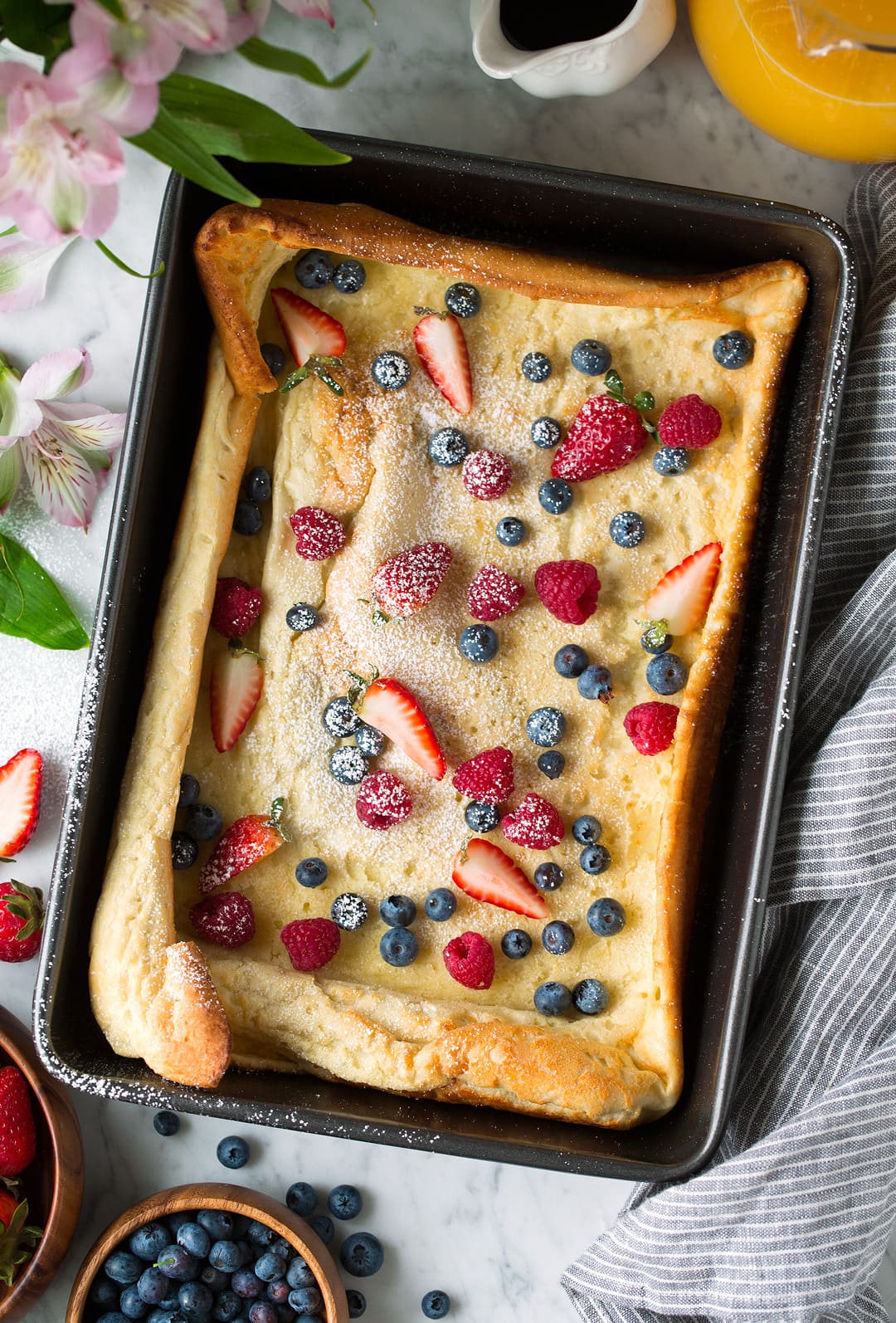 German Pancake in dark baking pan topped with powdered sugar and fresh fruit