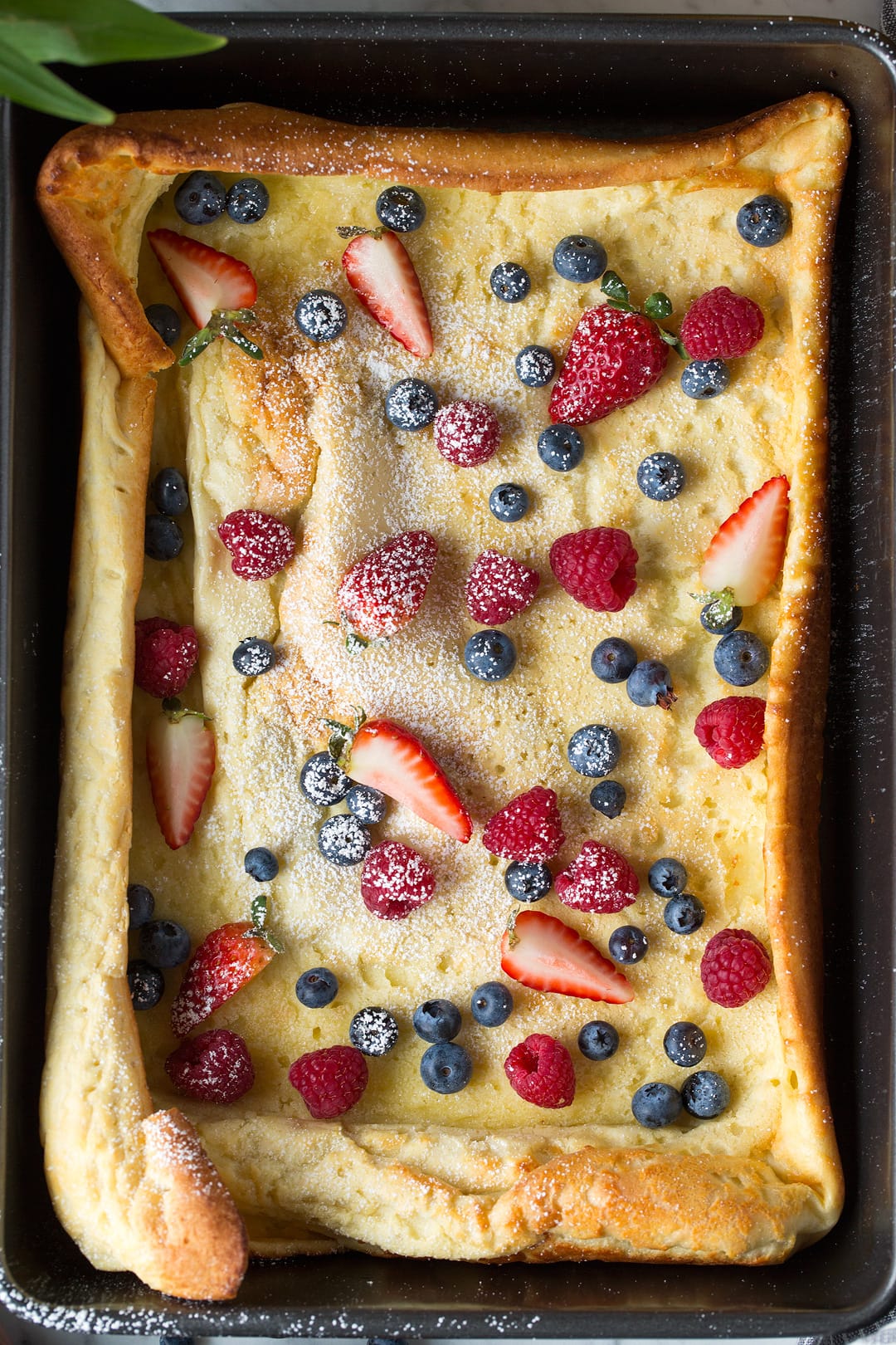 German Pancake in baking pan topped with fresh sliced fruit and powdered sugar