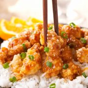 Up close photo of Chinese Orange Chicken with chopsticks grabbing one piece of chicken