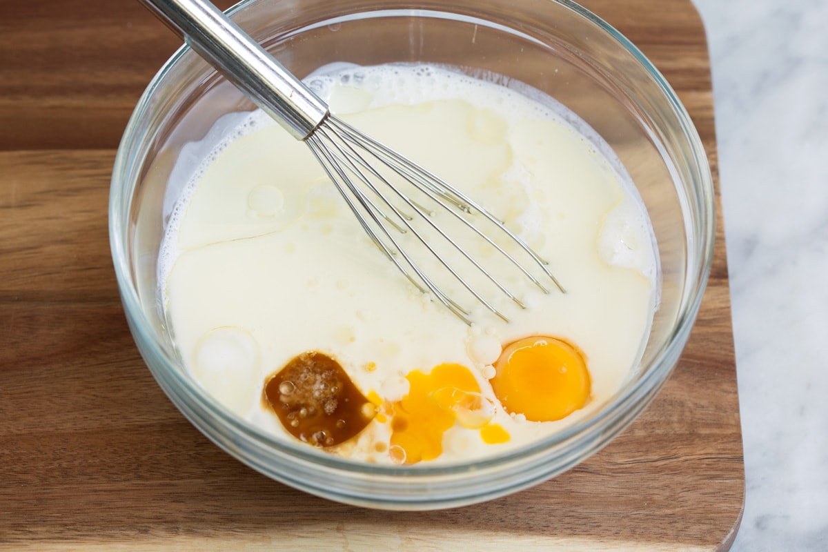 Whisking wet ingredients for belgian waffle batter in a glass mixing bowl.