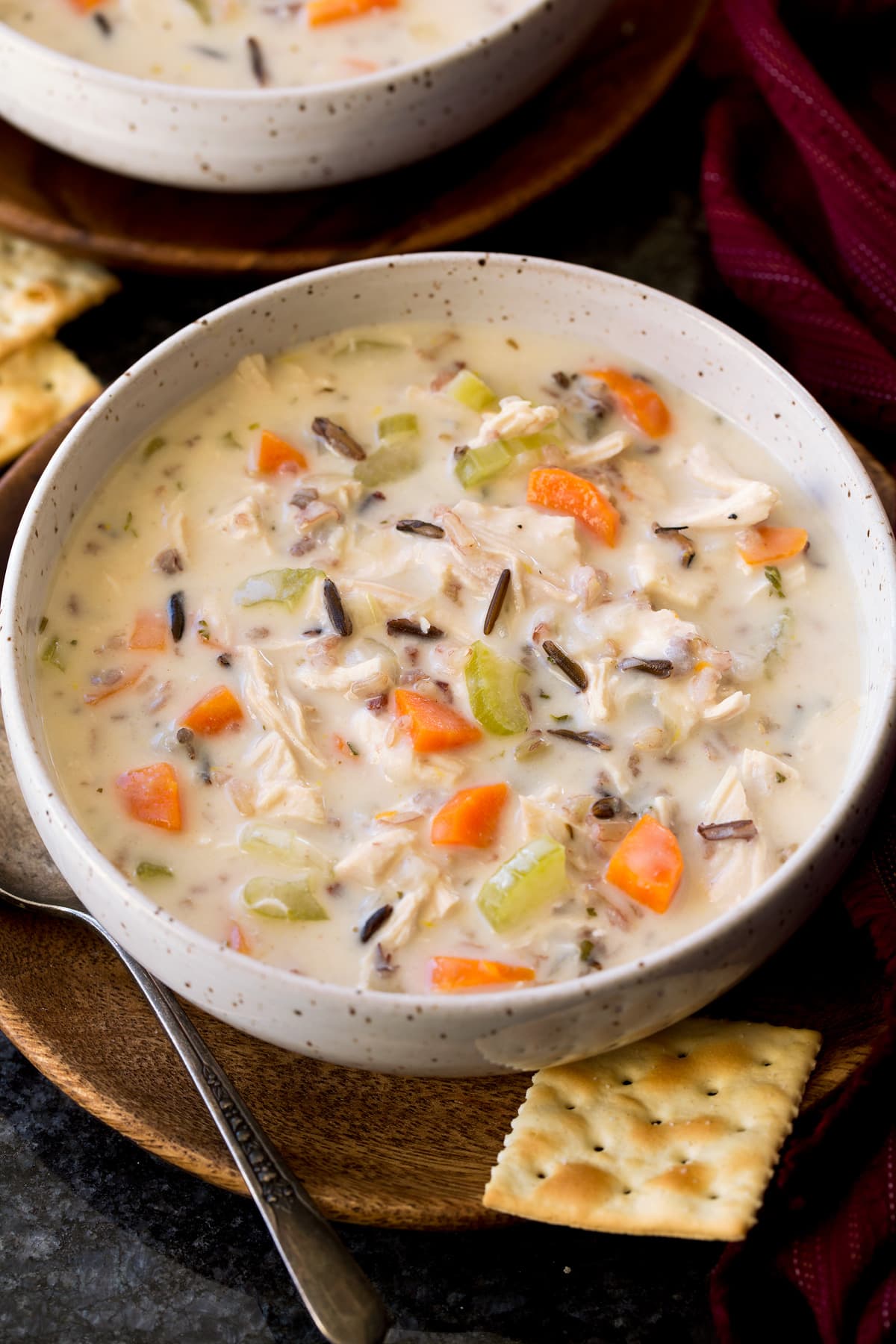 Serving of chicken and wild rice soup shown in a white bowl over a wooden plate on a black surface.