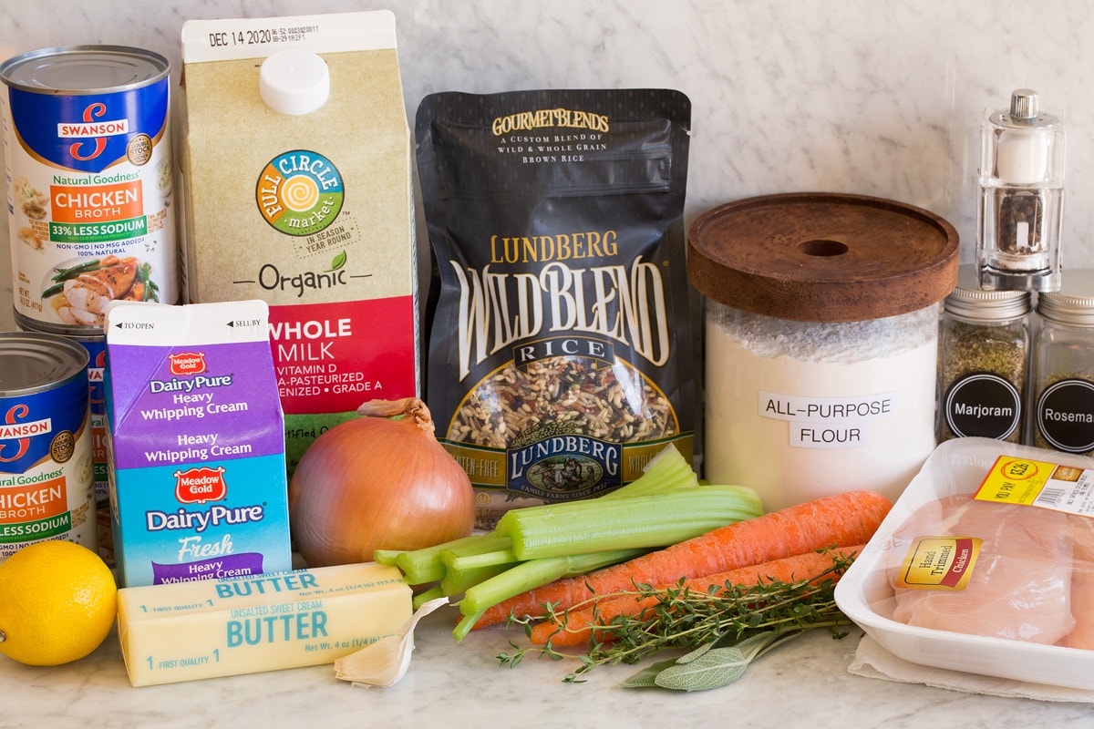 Image of ingredients used to make chicken and wild rice soup. Includes wild rice, chicken breasts, herbs, carrots, celery, onion, garlic, butter, milk, cream, lemon, flour, salt, pepper and chicken broth.