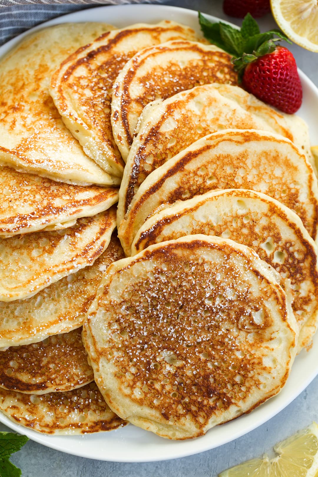 stack of lemon ricotta pancakes swirled around on a large plate garnished with lemon slices and strawberries