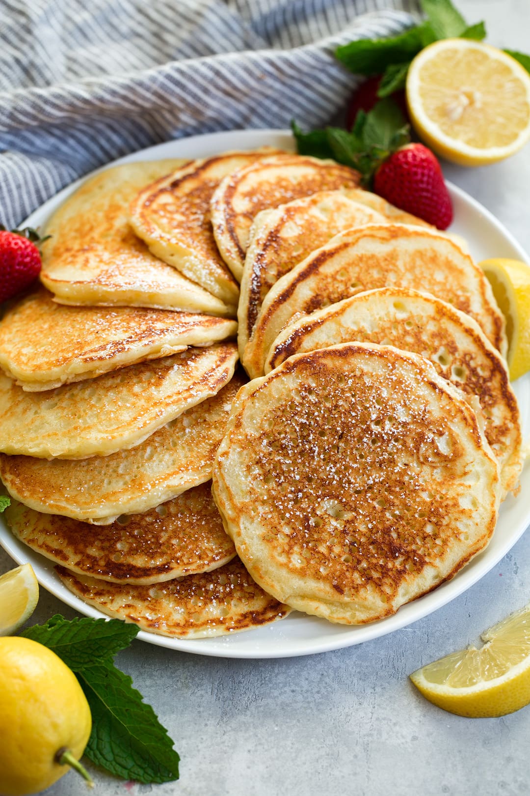stack of lemon ricotta pancakes swirled around on a large plate garnished with lemon slices and strawberries