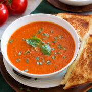 Serving of tomato basil soup shown close up in a white bowl with a grilled cheese to the side.