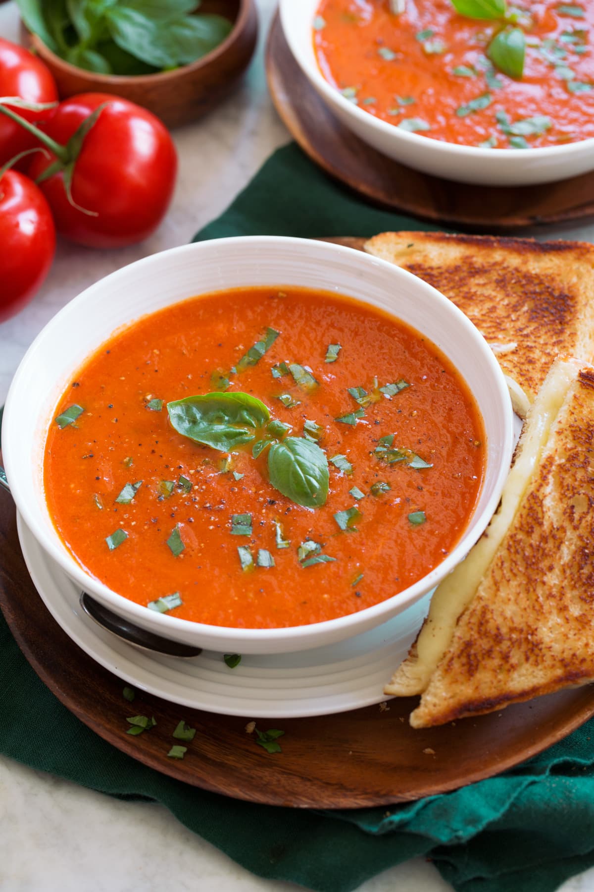 Serving of tomato basil soup shown close up in a white bowl with a grilled cheese to the side.