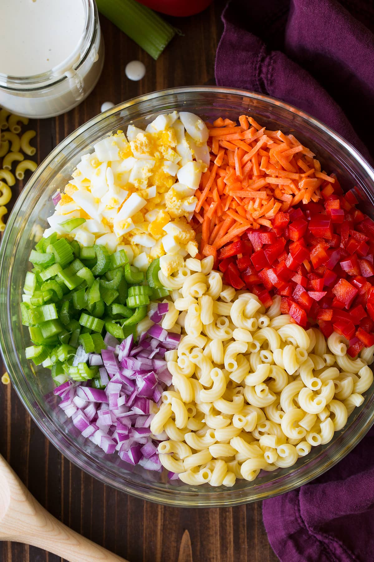 Macaroni salad ingredients in a glass bowl before tossing together.
