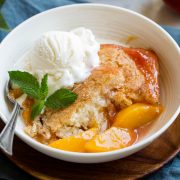 Serving of homemade peach cobbler in a white serving bowl topped with vanilla ice cream and mint.