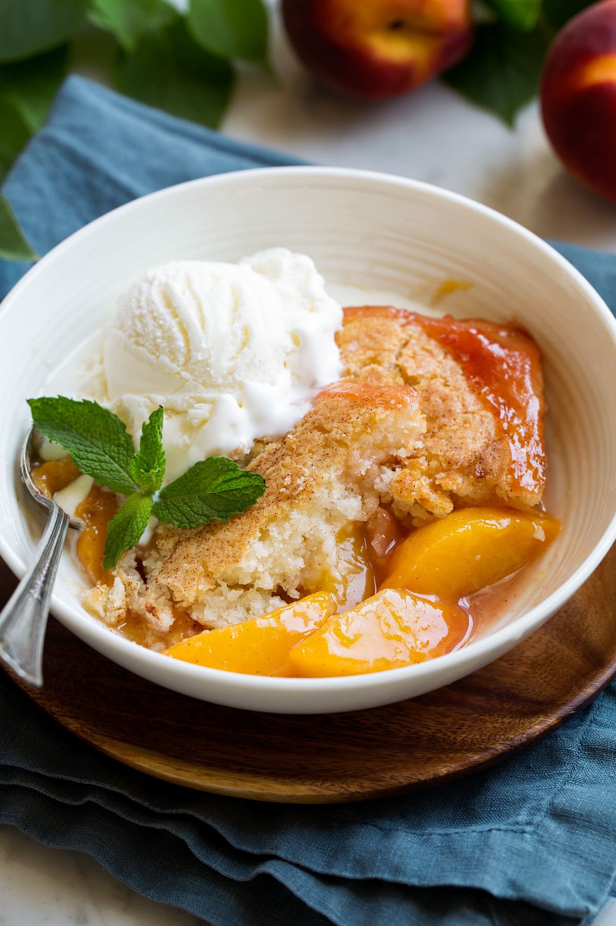 Serving of homemade peach cobbler in a white serving bowl topped with vanilla ice cream and mint.