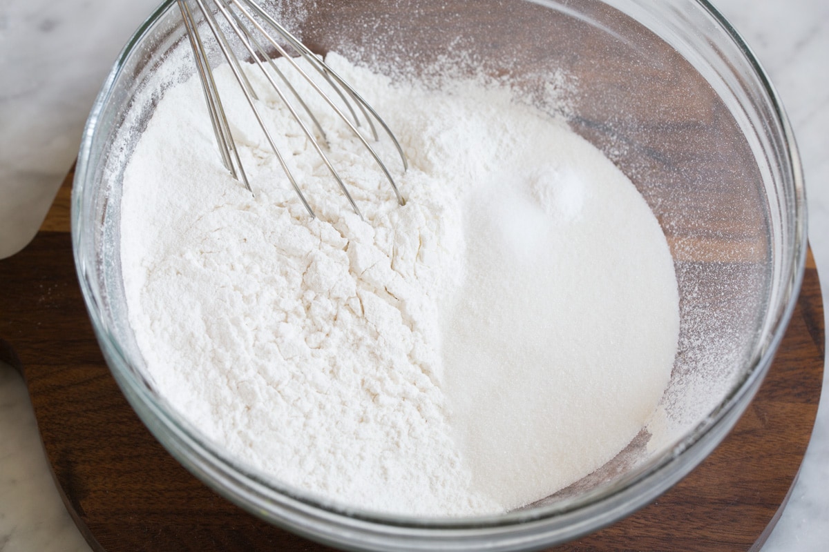 Whisking flour and sugar in a baking dish to prepare fluffy biscuit topping for peach cobbler.