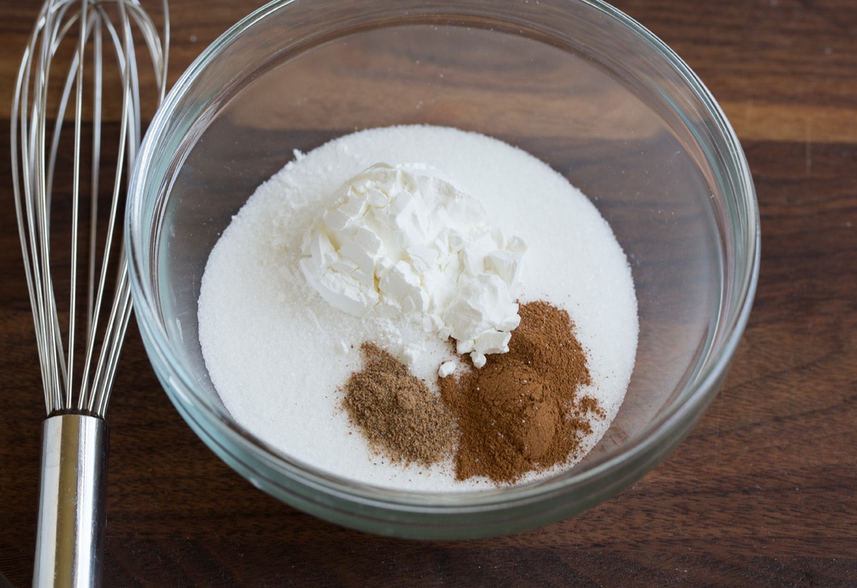 Showing the steps to making peach cobbler. In a mixing bowl whisking together sugar, cinnamon, nutmeg and cornstarch.