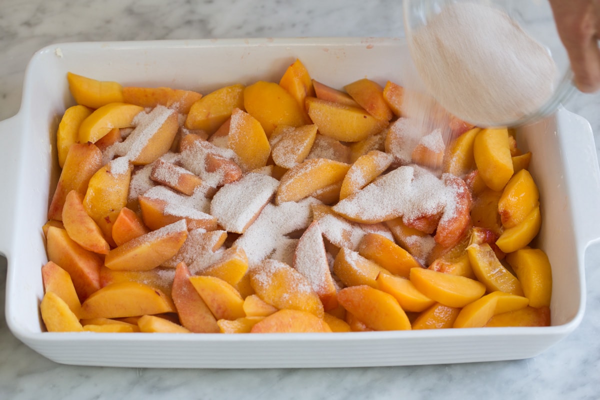 Pouring sugar mixture over peaches in baking dish.