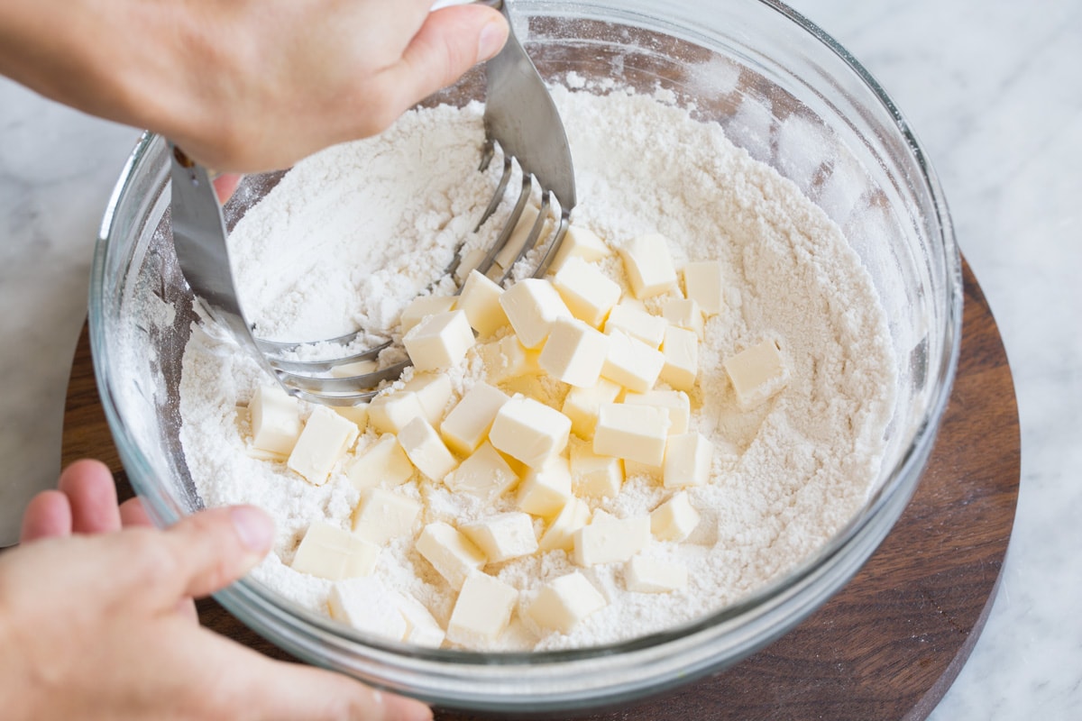 Cutting butter into flour mixture in glass mixing bowl with a pastry cutter.
