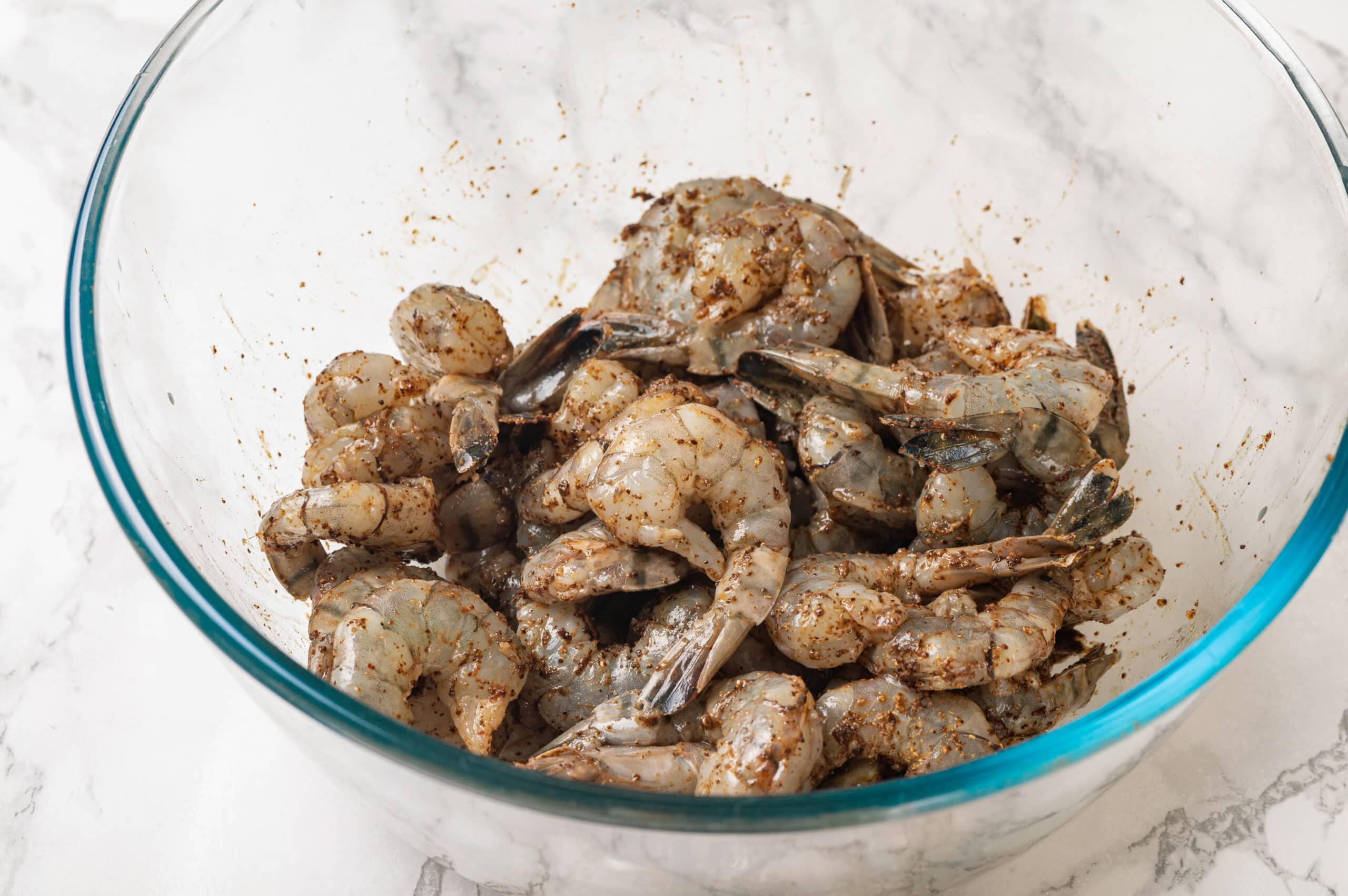 Tossing raw shrimp with Mexican spices in a glass bowl.