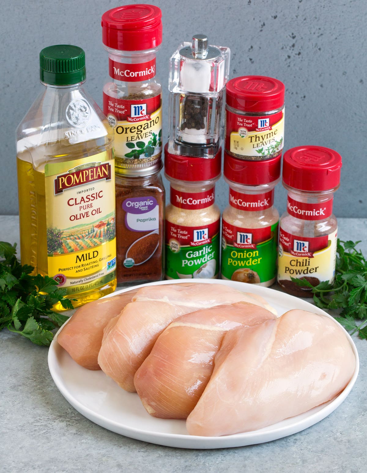 Ingredients needed to make oven baked chicken breast shown here including small chicken breasts, chili powder, paprika, garlic powder, onion powder, thyme, oregano, salt pepper, olive oil and parsley.