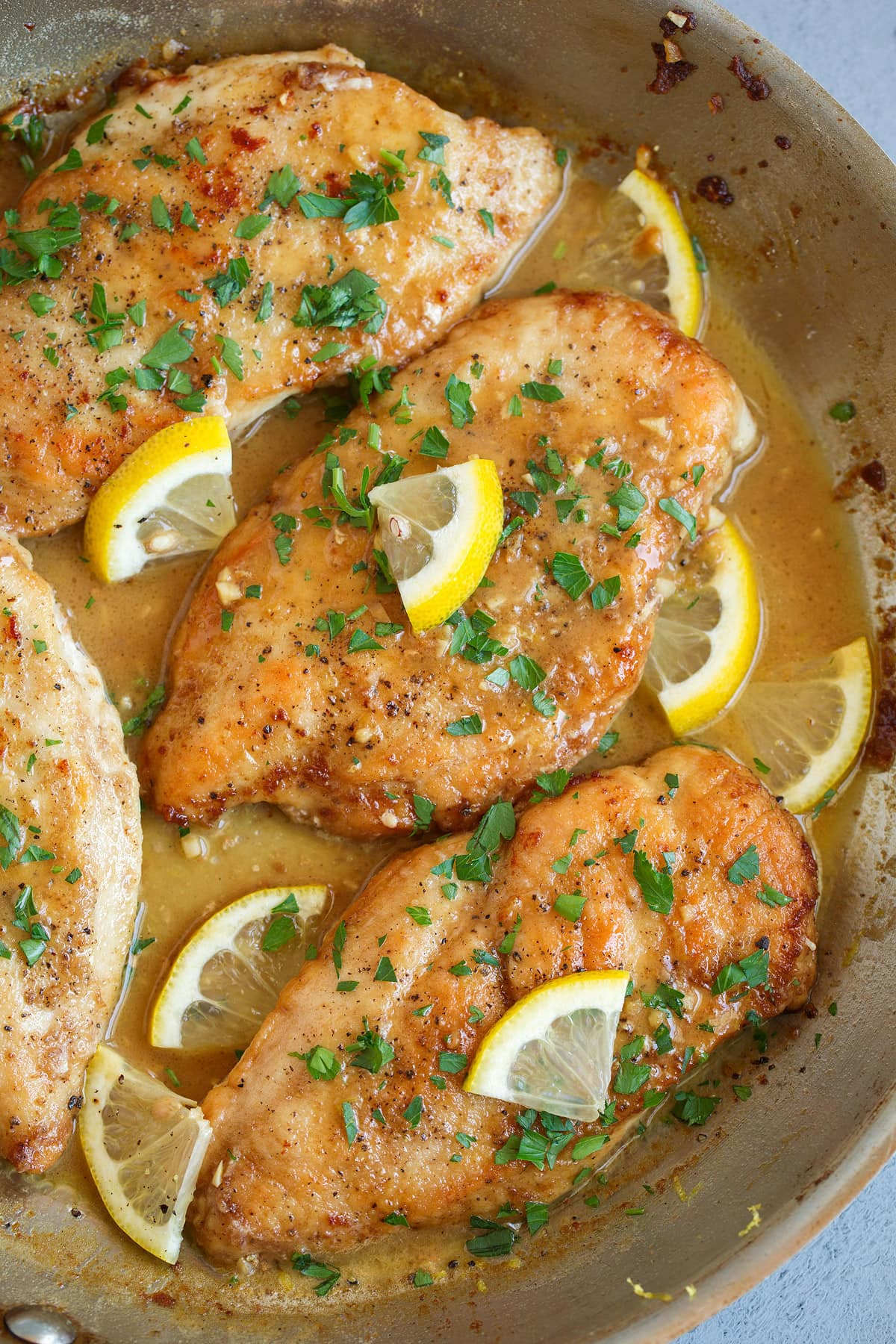 Lemon Chicken in a skillet. Chicken cutlets are pan seared and golden brown and served in a rich butter sauce, garnished with parsley.