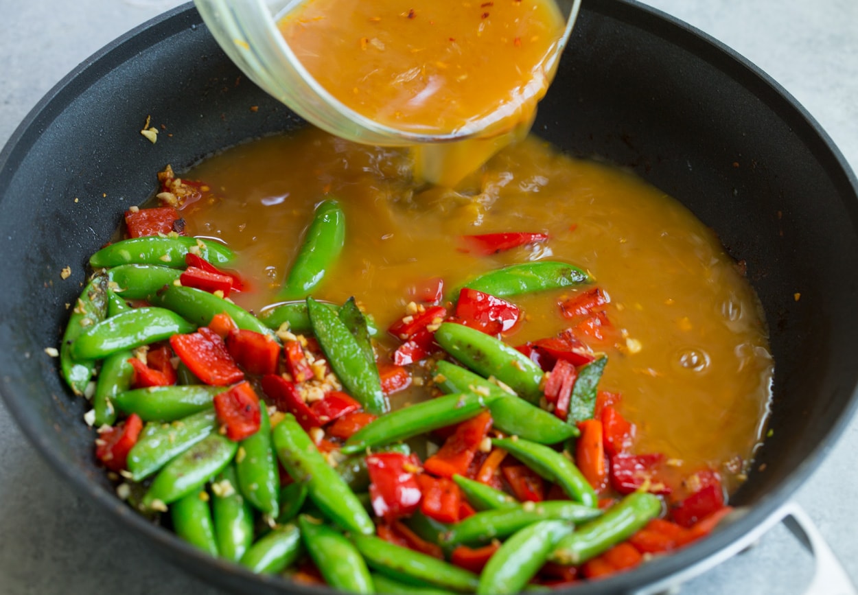 Orange Garlic Shrimp adding orange stir fry sauce to skillet along with veggies