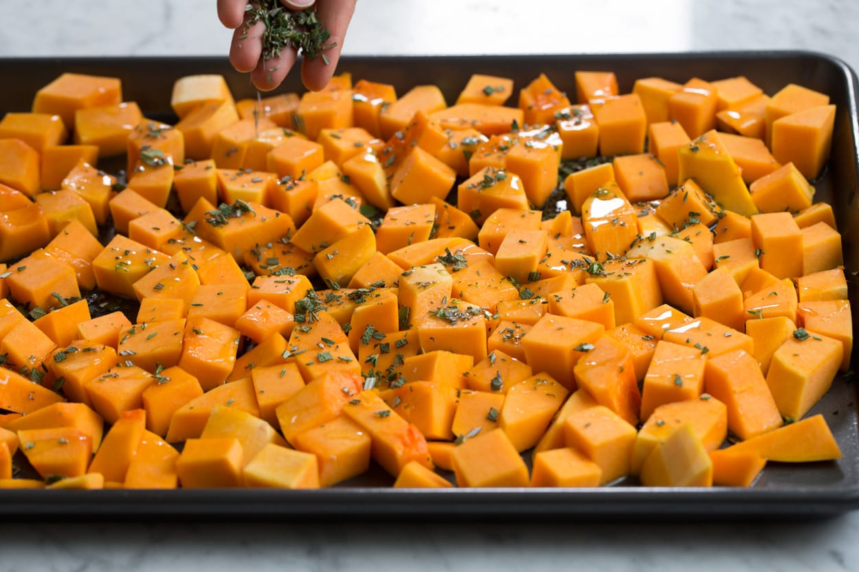 Drizzling butternut squash on a baking sheet with olive oil and sprinkling with herbs.