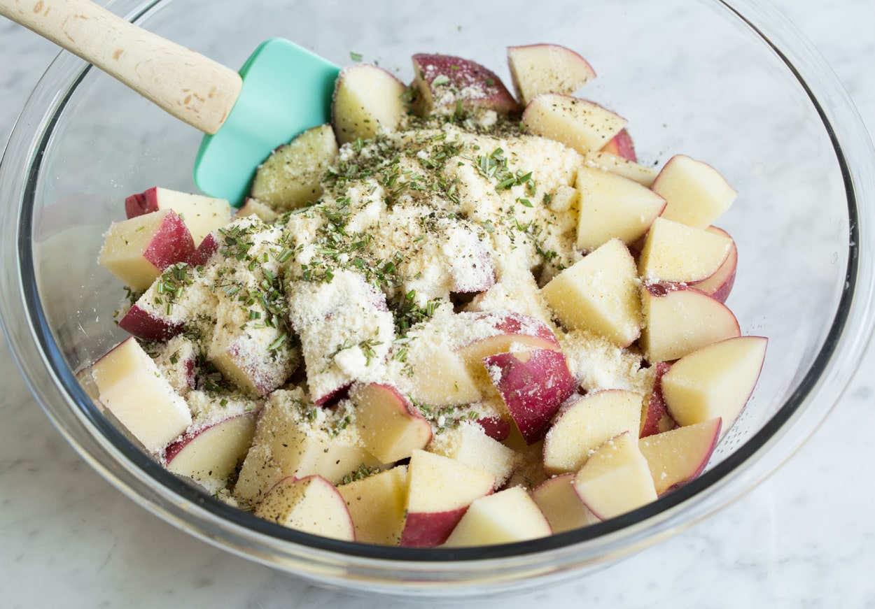 Showing how to roast potatoes. Tossing potato chunks in a bowl with oil, garlic and herbs.