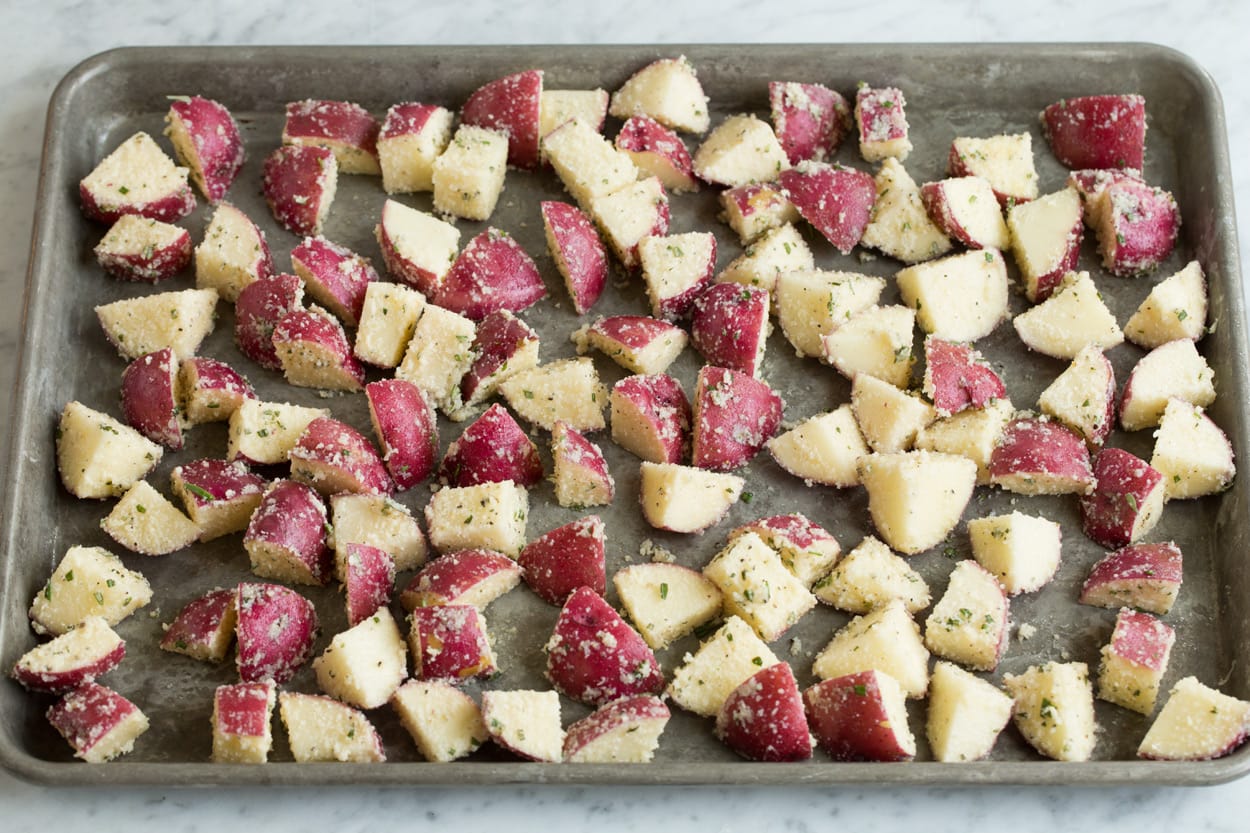 Potato cubes tossed with parmesan on a baking sheet to roast.