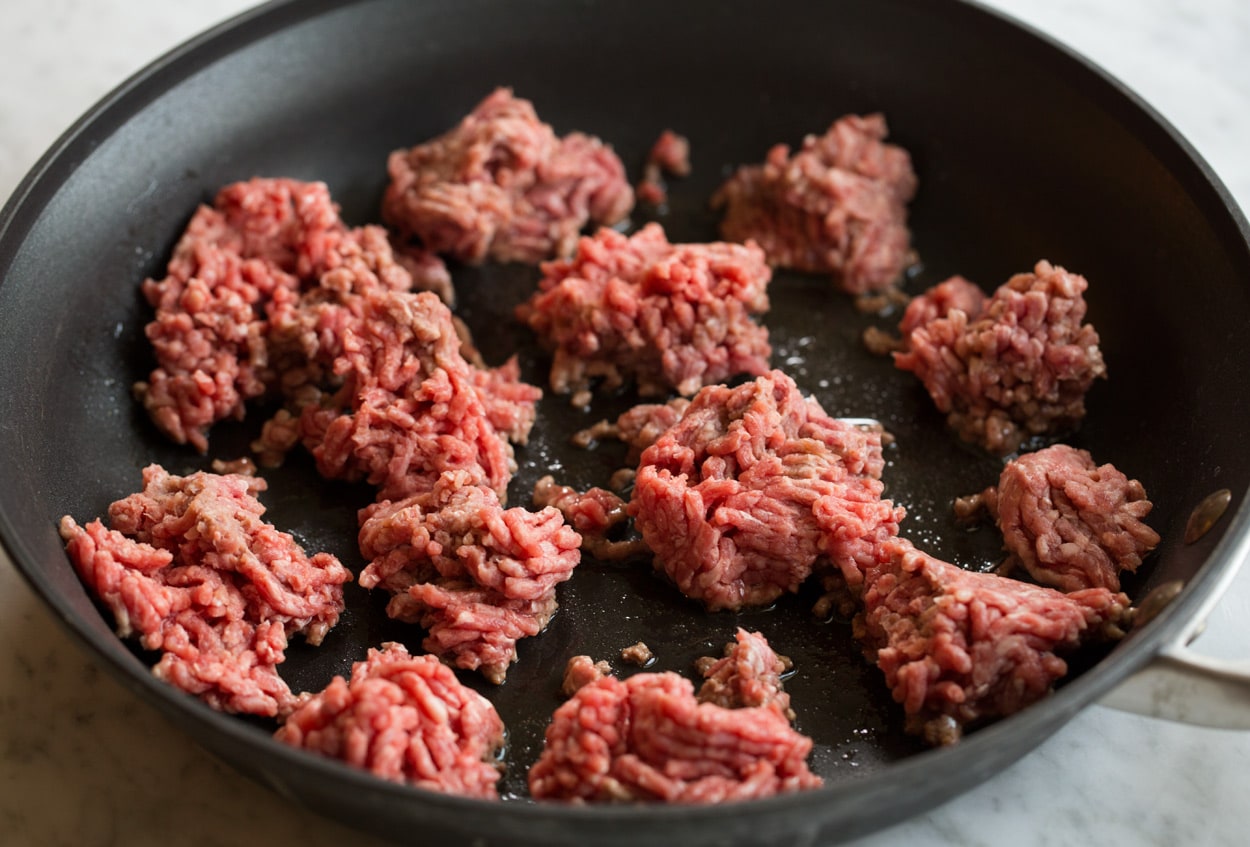 Showing how to make spaghetti sauce, browning beef in dark non-stick skillet in portions.