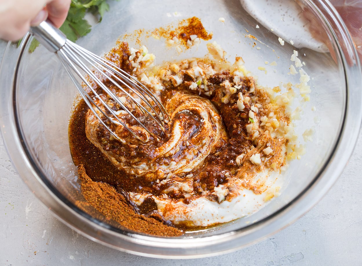 Showing how to make Tandoori Chicken marinade. Whisking yogurt, spices, garlic and ginger in a glass mixing bowl.