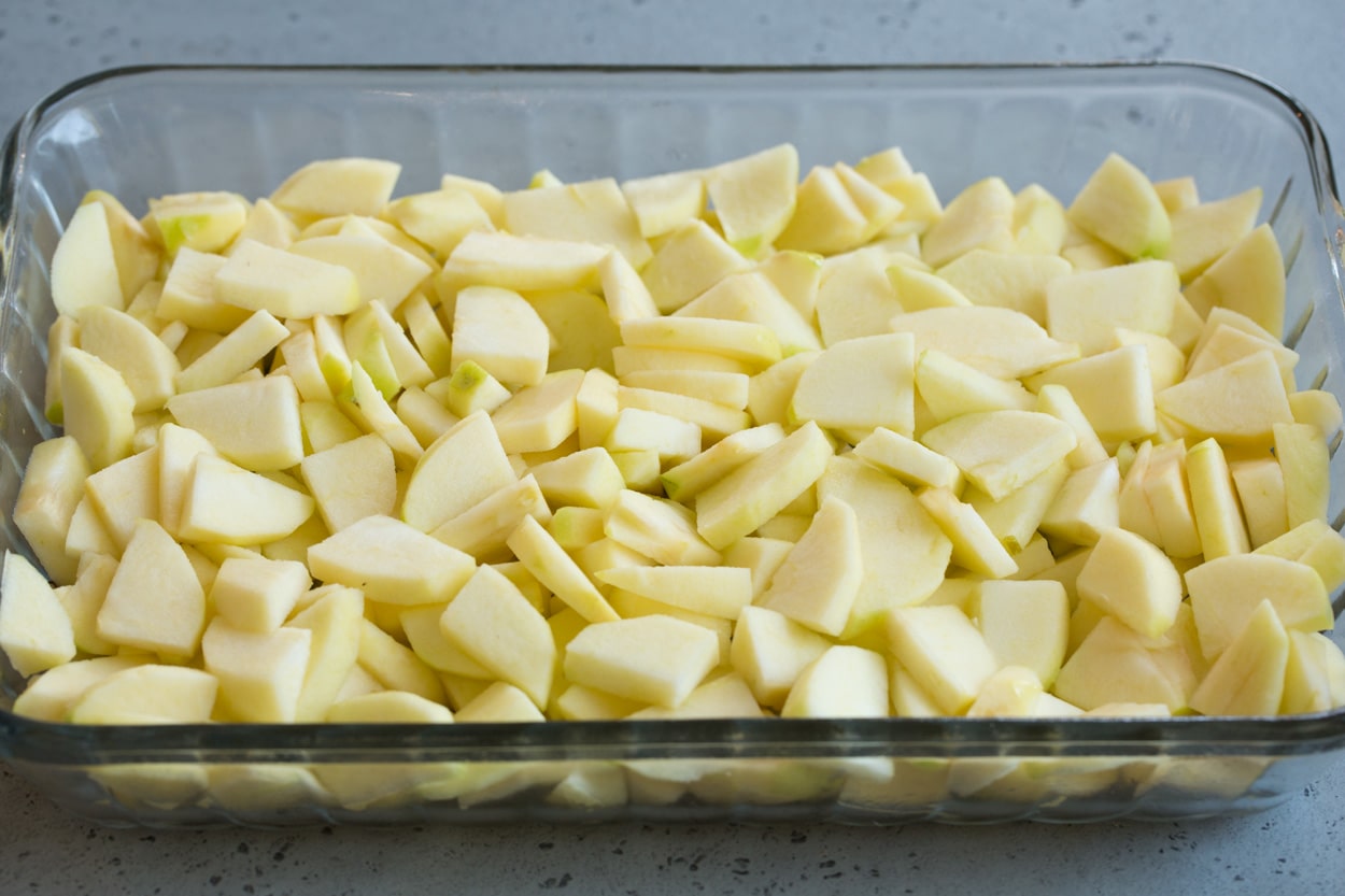 How to make apple cobbler shown here pouring sugar mixture over apples in baking dish