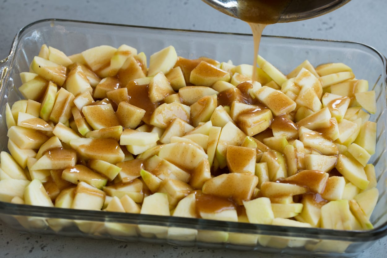 apple cobbler shown here pouring sugar mixture over apples in baking dish