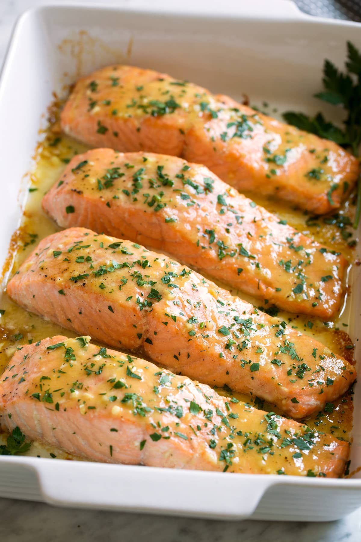 Four salmon fillets in a baking dish brushed with a sweet and tangy, buttery honey mustard sauce.