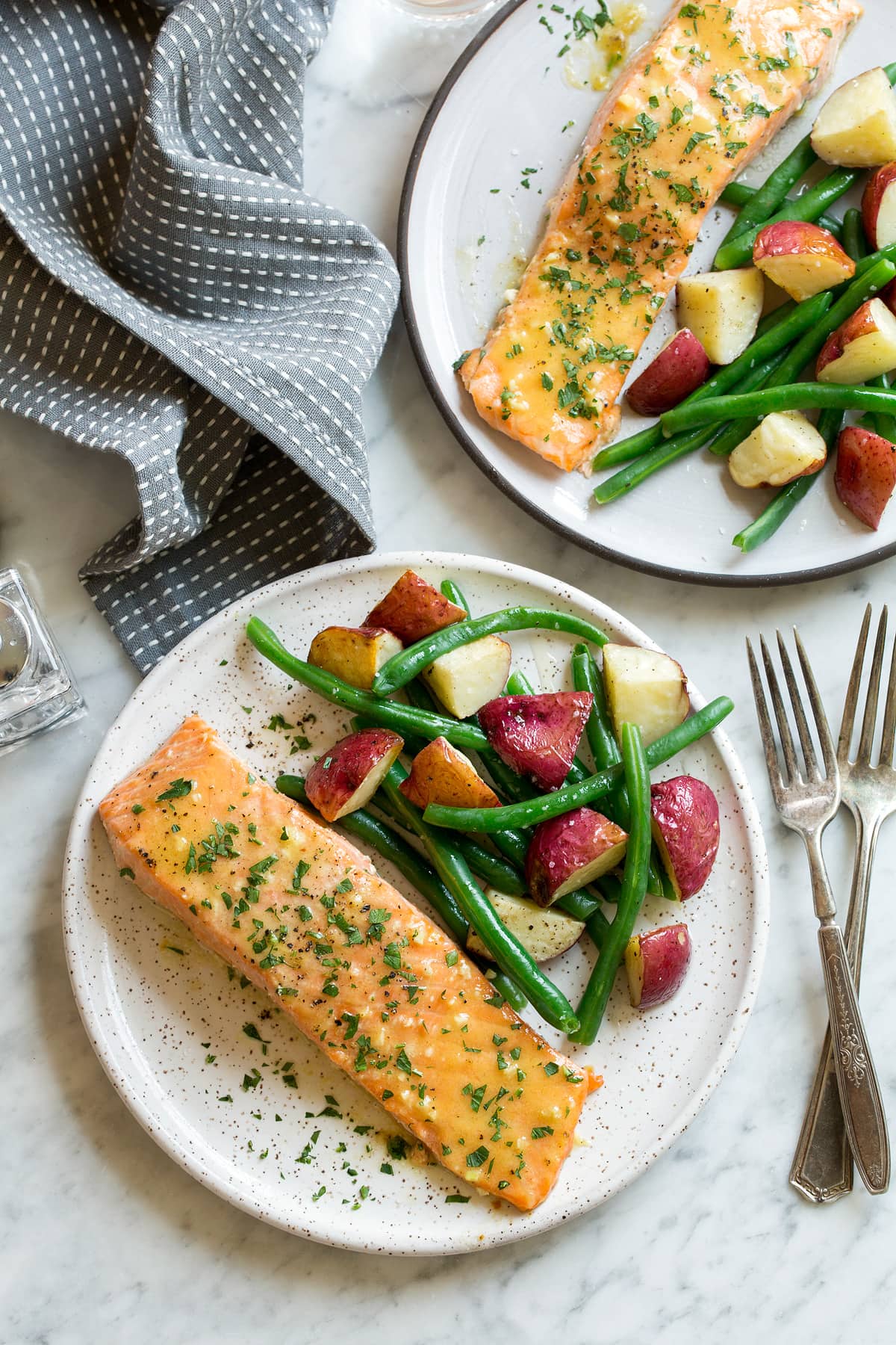Overhead image of two servings of Baked Salmon with Buttery Honey Mustard Sauce on white serving plates set over a marble surface.