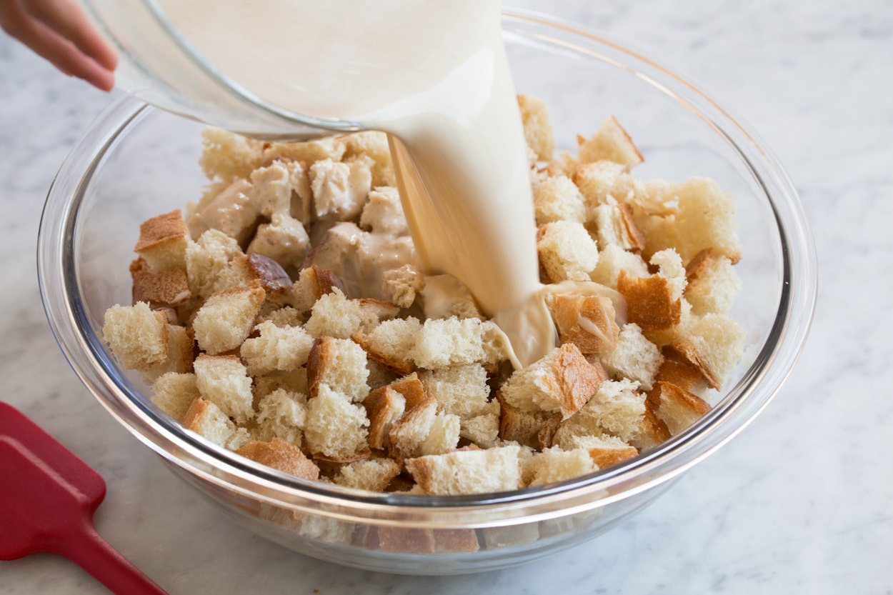 pouring custard mixture over bread cubes for bread pudding
