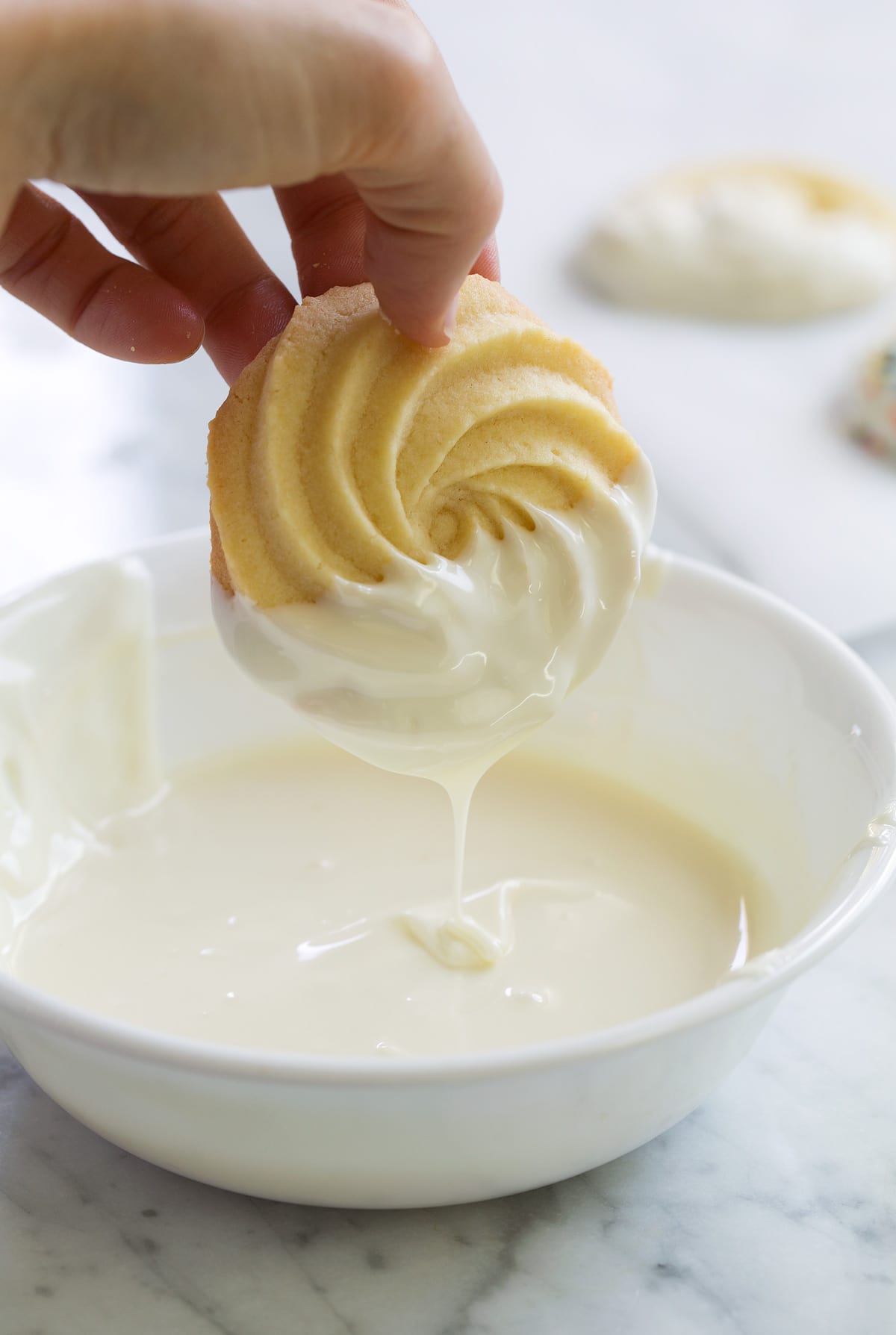 Dipping butter cookie in white chocolate melts in a small bowl.