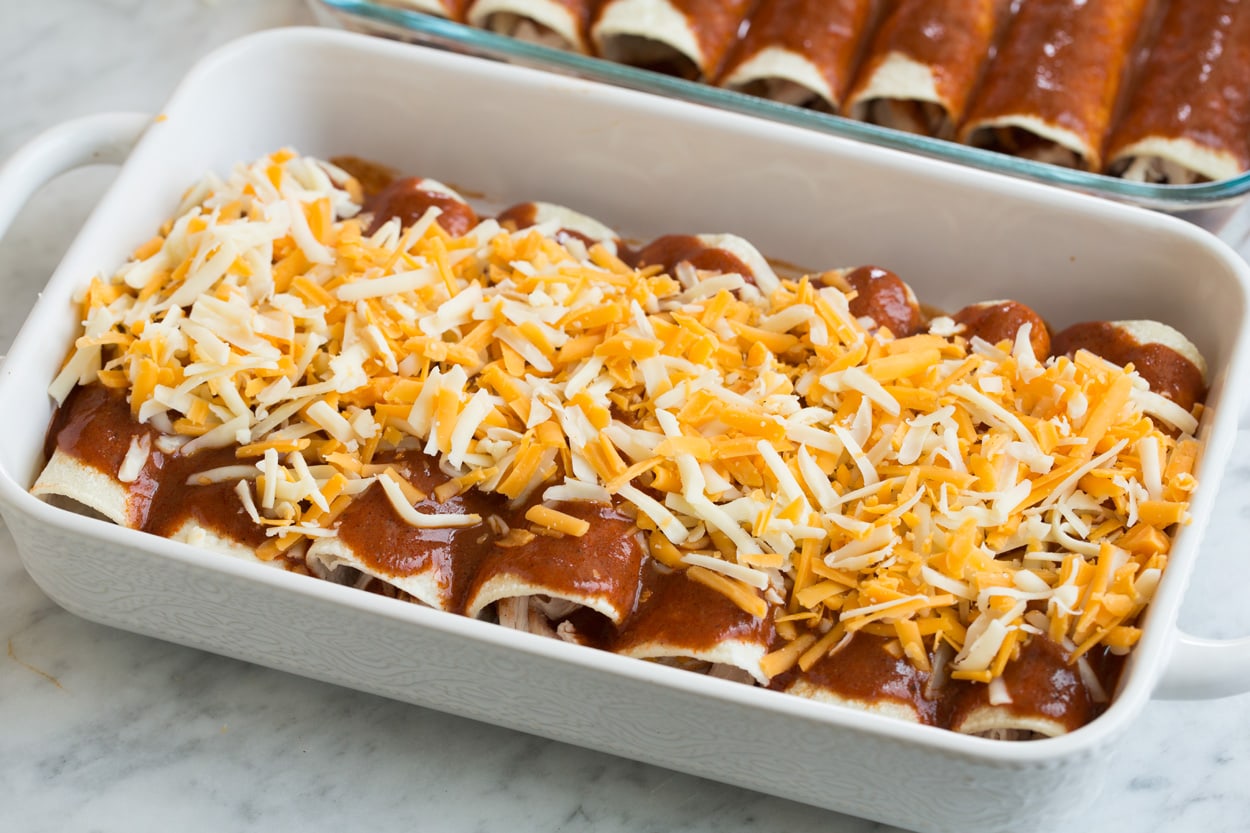 Chicken enchiladas in baking dish with cheese and sauce on top before baking