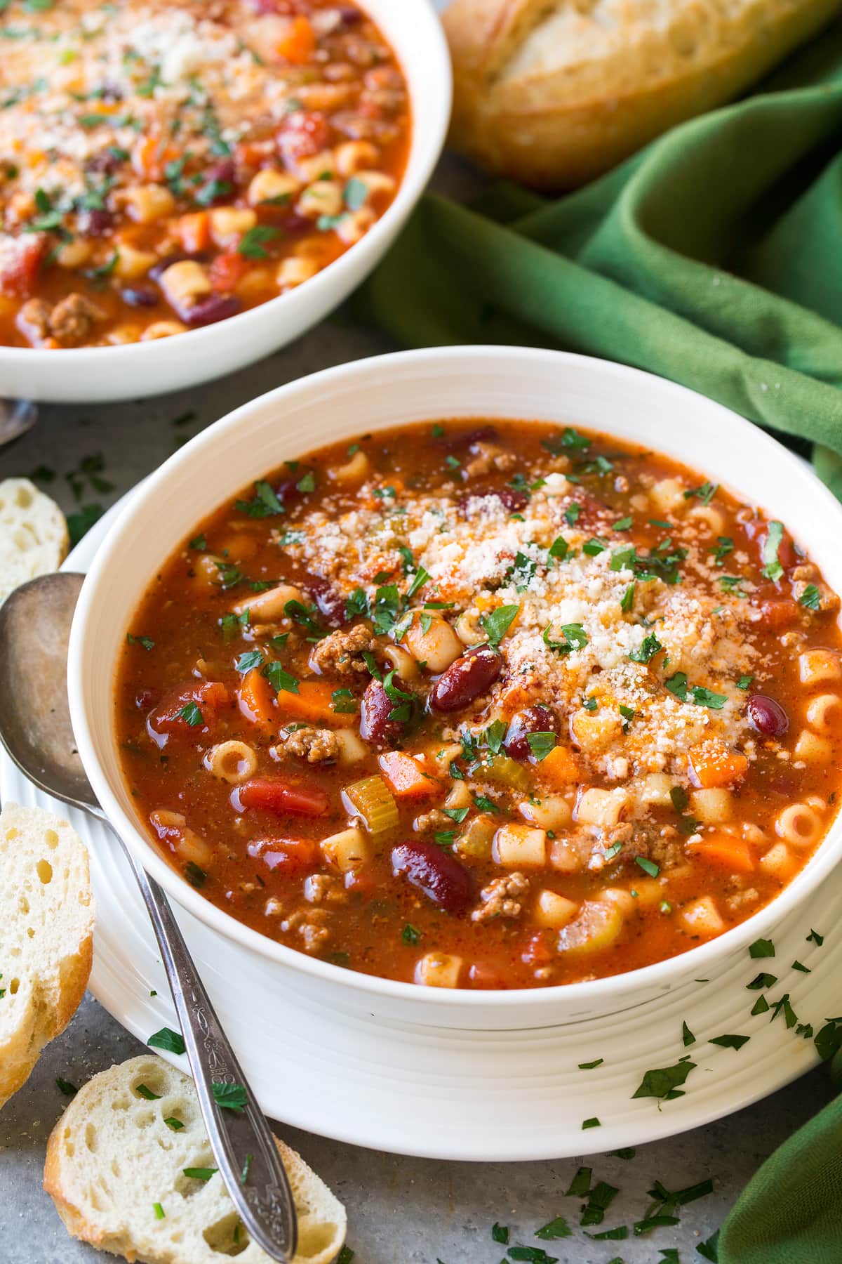 Two servings of Pasta e Fagioli Soup in white serving bowls set over white plates. Served with french bread on the side.