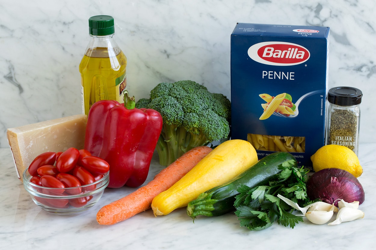 Pasta Primavera ingredients shown here penne olive oil red onion carrots broccoli bell pepper squash zucchini garlic tomatoes parmesan lemon italian seasoning
