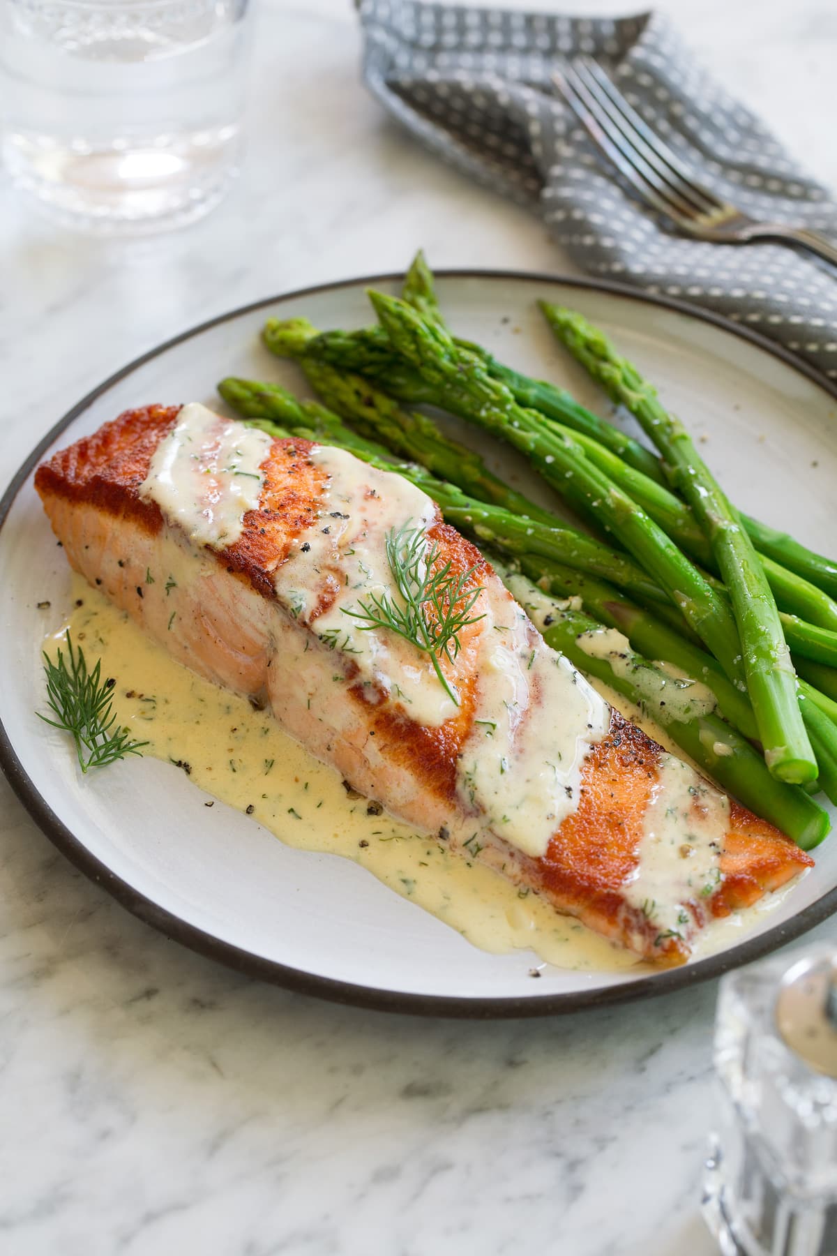 Salmon fillet on a white plate set over a marble surface. Topped with dijon sauce and served with a side of asparagus. 
