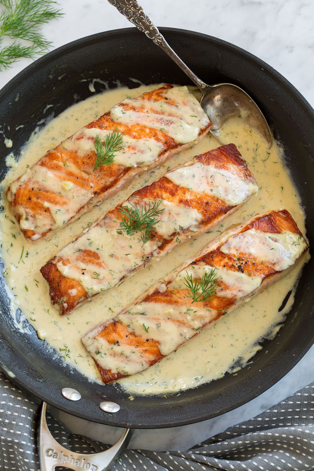 Three salmon fillets in a skillet with a creamy dijon sauce.