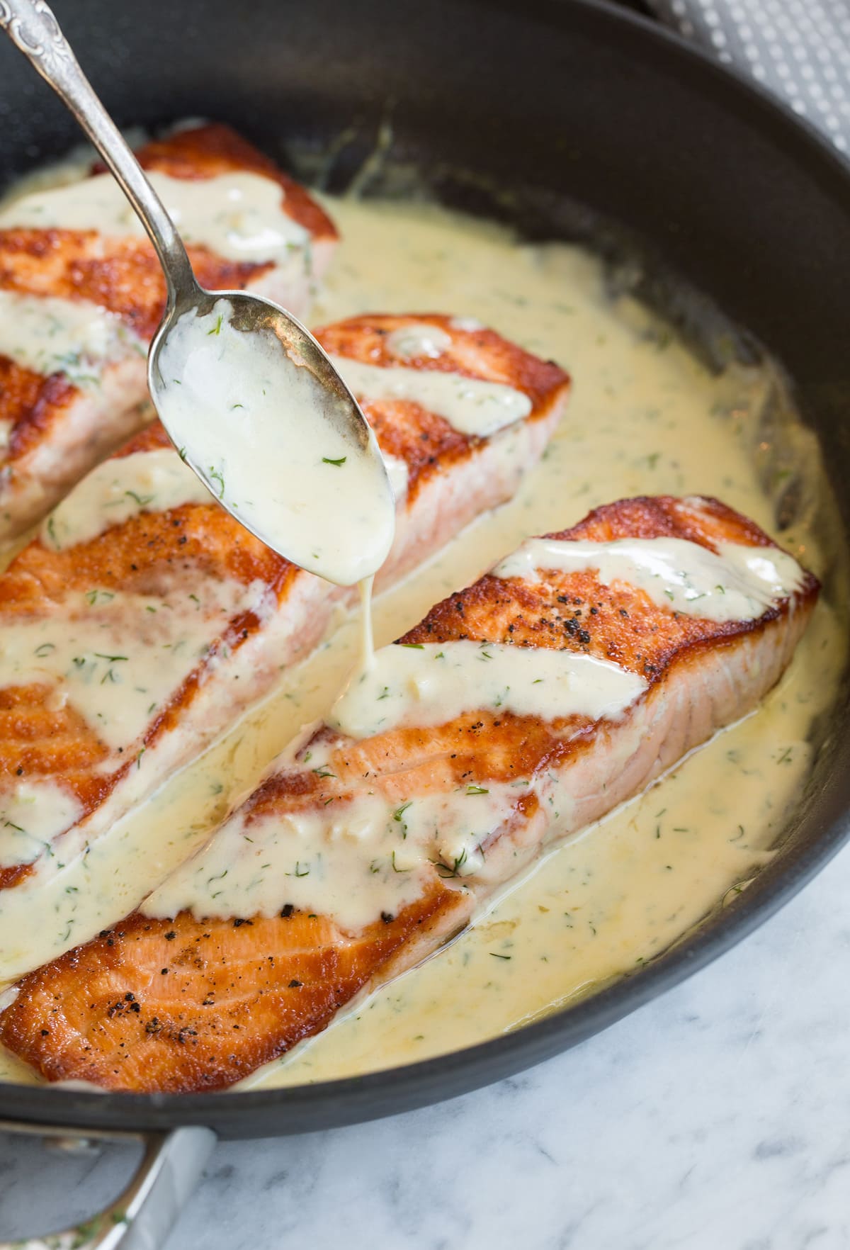 Spooning sauce over a fillet of salmon in a skillet.