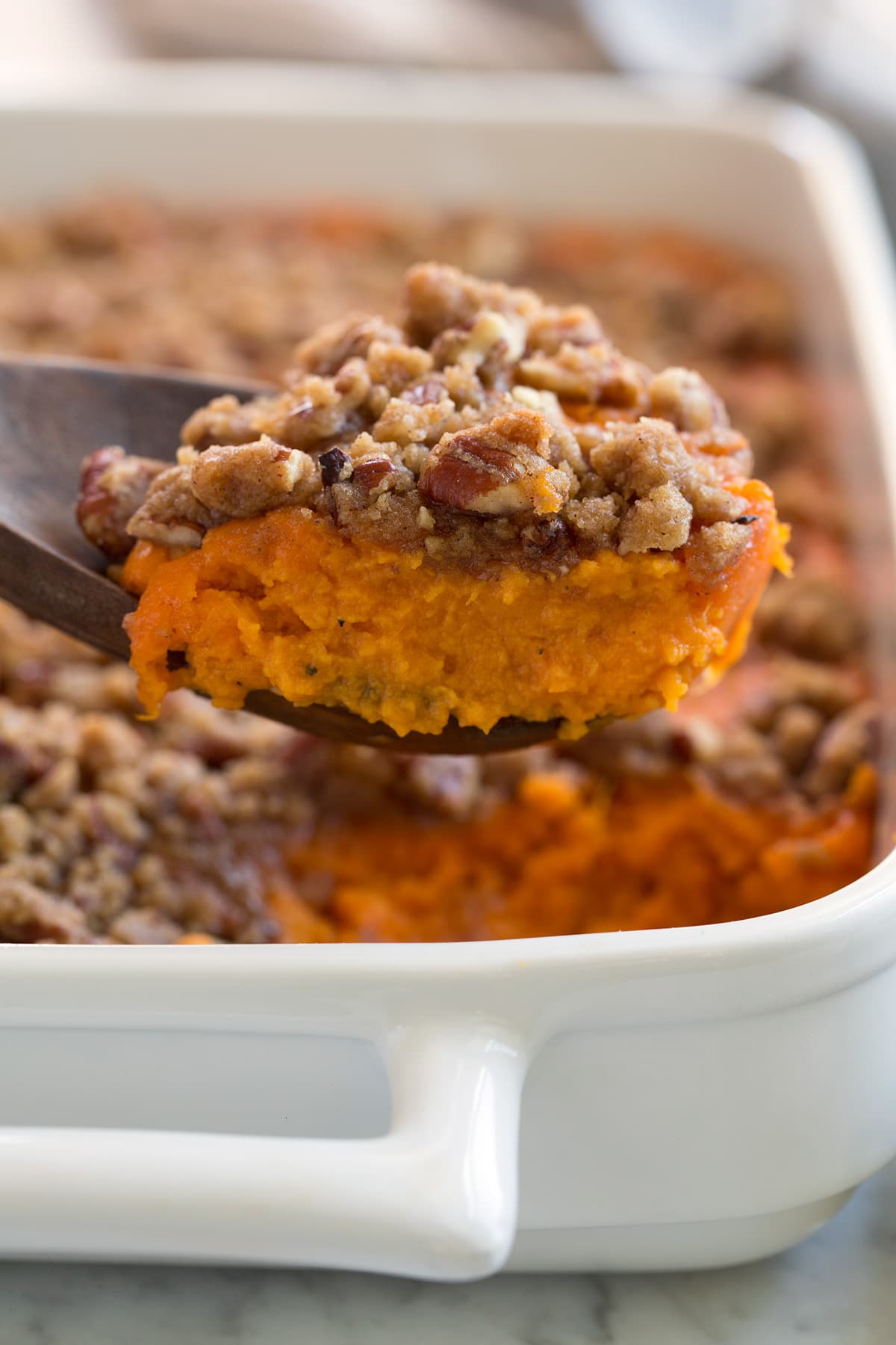 Close up image of a scoop of sweet potato casserole showing creamy orange sweet potato layer and a crisp, sugary pecan crumble.