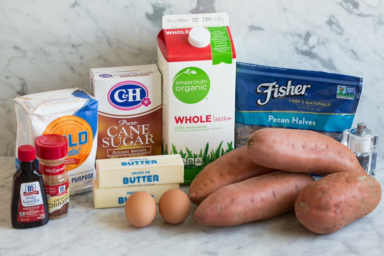 Sweet Potato Casserole ingredients shown sitting on a marble surface. Includes sweet potatoes, pecans, salt and pepper, milk, butter, eggs, brown sugar, flour, cinnamon and vanilla.