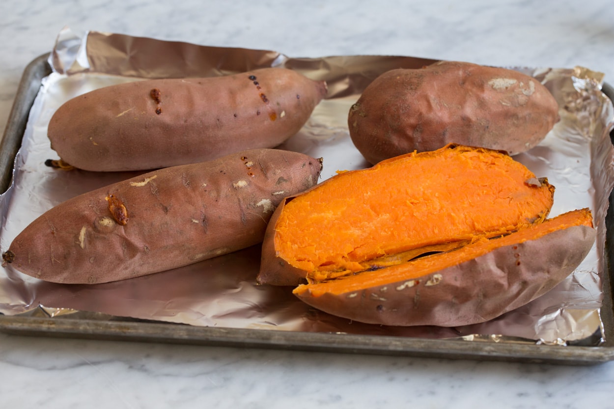 Four baked sweet potatoes shown here, one sliced open. Before adding to sweet potato casserole.