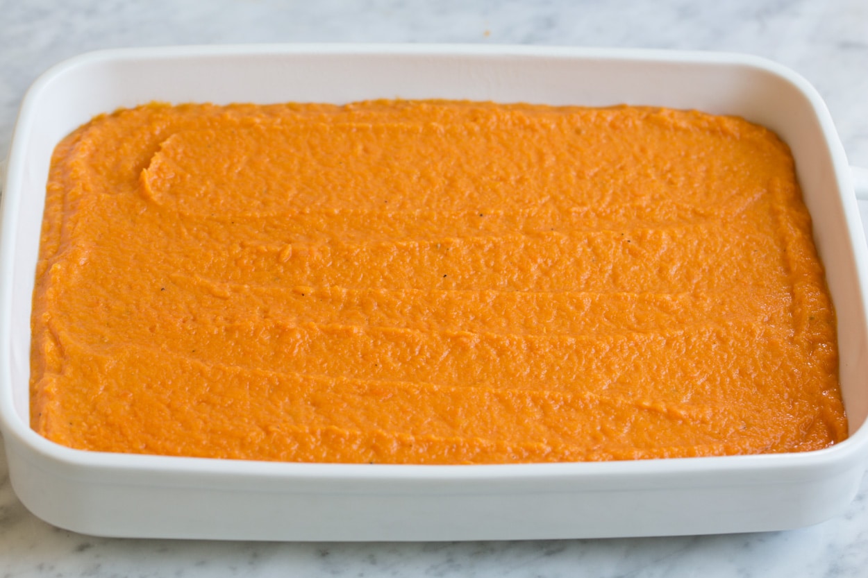 Sweet potato layer spread into white ceramic baking dish for sweet potato casserole.